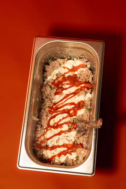 Tuna salad with mayo and sriracha drizzle in a stainless steel prep pan, served fresh in-house.