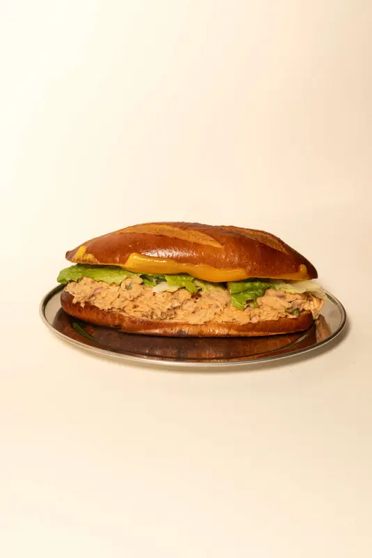 Tuna melt sub sandwich with lettuce and cheese on a toasted hoagie roll, served on a silver plate.