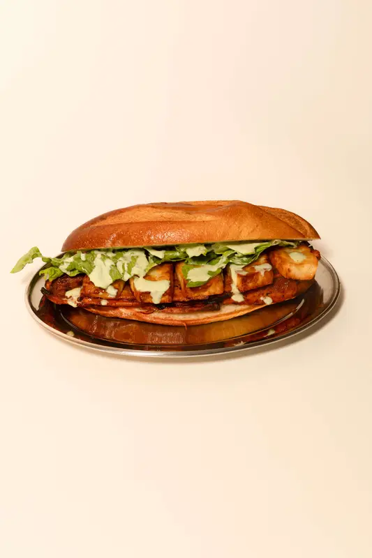 Grilled chicken sandwich on toasted hoagie roll with lettuce and creamy green sauce on a silver platter
