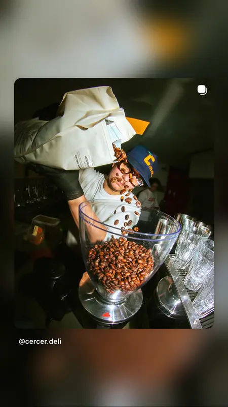 Barista pouring fresh coffee beans into grinder hopper at Cercer Deli café bar