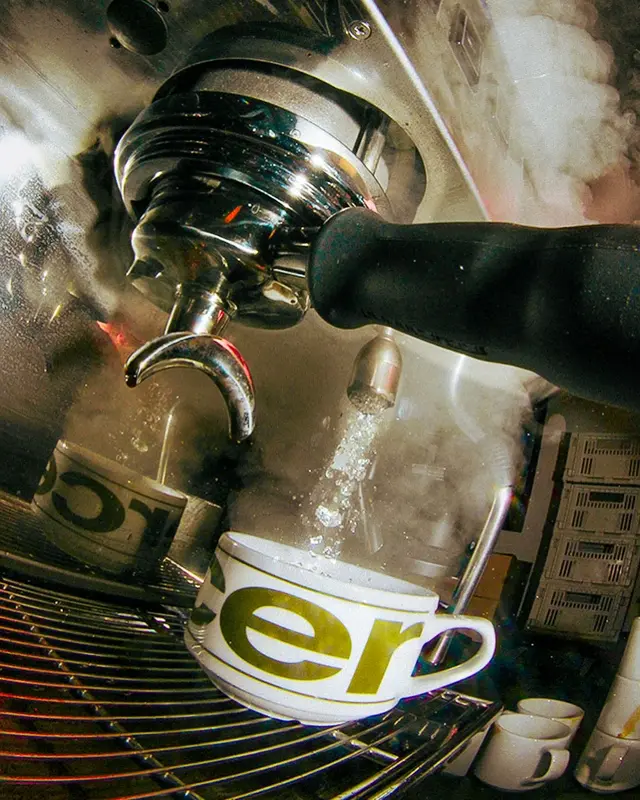 Espresso being brewed into an "ero" branded cup at a professional coffee machine with steam rising