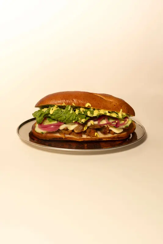 Loaded sub sandwich with melted cheese, pickled red onions, lettuce, mustard, and savory meat on a brioche roll