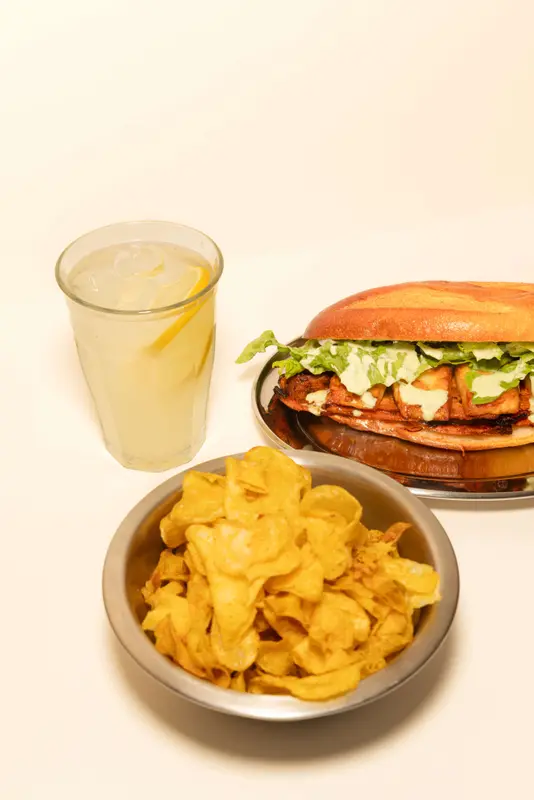 Grilled chicken sandwich with arugula on brioche bun, served with potato chips and fresh lemonade on ice